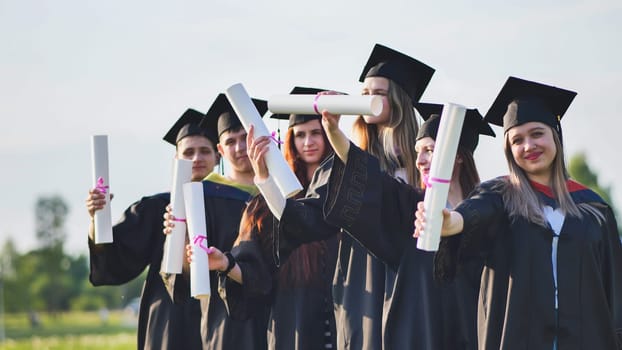 Cheerful graduates waving their diplomas on a sunny day