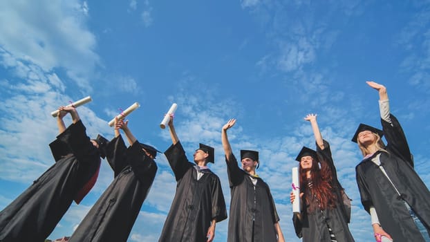 Cheerful graduates waving their diplomas on a sunny day