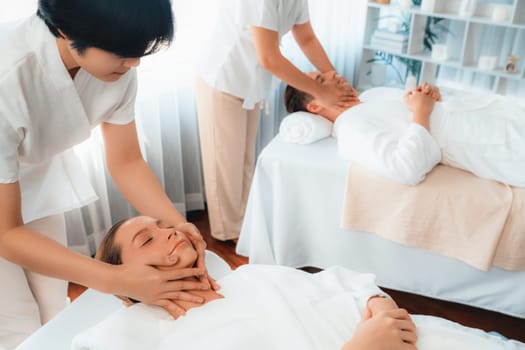 Caucasian couple enjoying relaxing anti-stress head massage and pampering facial beauty skin recreation leisure in dayspa modern light ambient at luxury resort or hotel spa salon. Quiescent