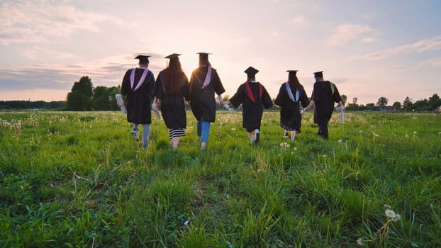 Six graduates in robes walk towards the sun