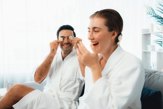 Blissful couple in bathrobe playing with cucumber and enjoying daylight ambiance spa salon resort or hotel during holiday. Pampering face spa and skincare treatment with essence relaxation. Quiescent