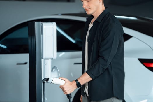 Young man travel with EV electric car to shopping center parking lot charging in downtown city showing urban sustainability lifestyle by green clean rechargeable energy of electric vehicle innards