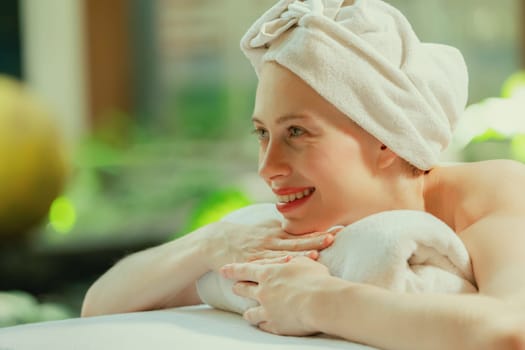 Closeup of beautiful women in white towel relaxes on spa bed surrounded by peaceful and calm nature. Young gorgeous female wearing white towel during waiting for body massage. Side view. Tranquility