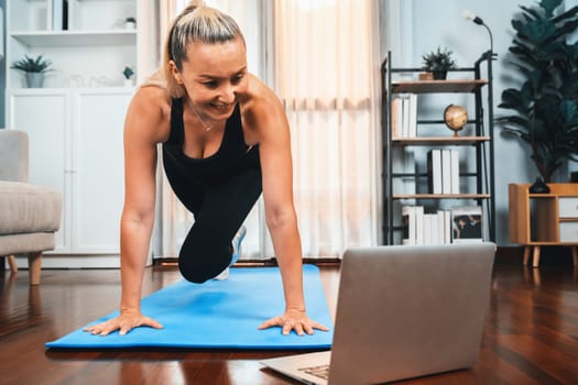 Athletic and active senior woman doing exercise on fit mat with plank climbing at home exercise while watching online exercising video as concept of healthy fit body lifestyle after retirement. Clout