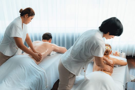 Caucasian couple customer enjoying relaxing anti-stress spa massage and pampering with beauty skin recreation leisure in day light ambient salon spa at luxury resort or hotel. Quiescent