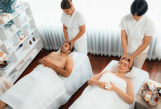 Caucasian couple enjoying relaxing anti-stress head massage and pampering facial beauty skin recreation leisure in dayspa modern light ambient at luxury resort or hotel spa salon. Quiescent