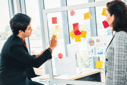 Business people work on project planning board in office and having conversation with coworker friend to analyze project development . They use sticky notes posted on glass to make it organized. Jivy