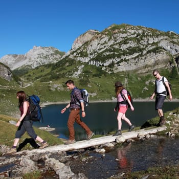 A group of teenagers crosses a footbridge during a hike in the mountains