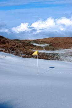 yellow flag on a snow covered links golf course in ireland in winter