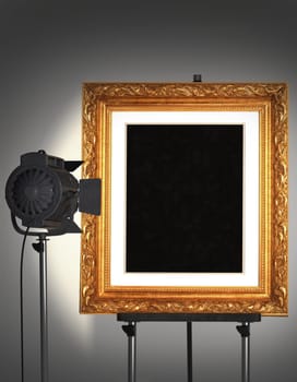 Empty gold frame being lit by a spotlight sitting on an easel.