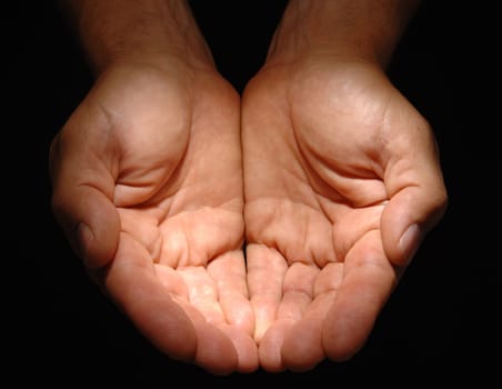 Close up of a man's cupped hands under a spotlight on a black background.