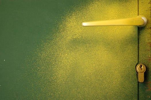 Yellow paint sprayed over green metal door and handle. Abstract background.