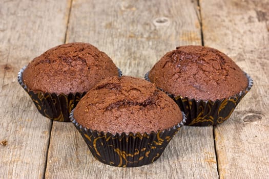 Three chocolate muffins on a wooden plank