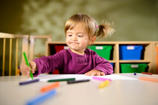 Little girl having fun at school and drawing with colors in kindergarten