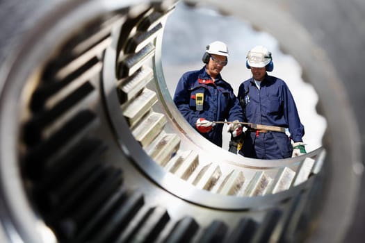 two mechanics, engineers seen through a large cogwheels axle