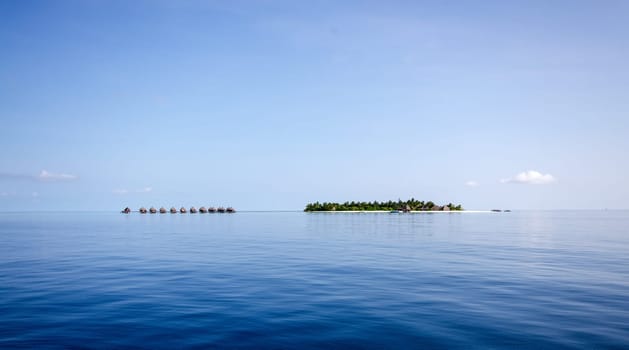 A small island in the Maldives with a number of cabins on stilts in the calm blue water