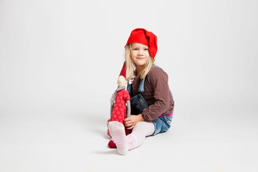 Studio portrait of happy smiling young girl holding Christmas elf doll while sitting