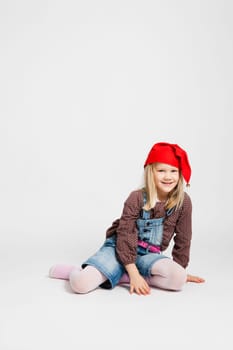 Studio portrait of happy smiling young girl wearing red Christmas hat and sitting in relaxed way