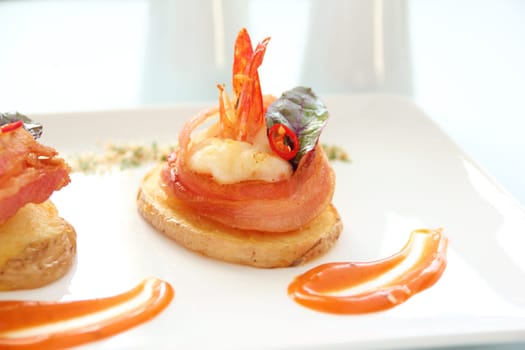 Delicious and delicate shrimps wrapped in bacon on potato slices with a spinach leaf.