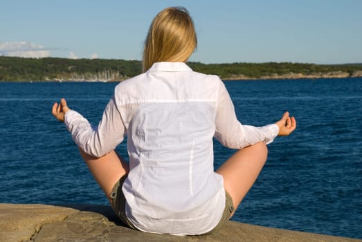 a woman sits on the coast, doing yoga