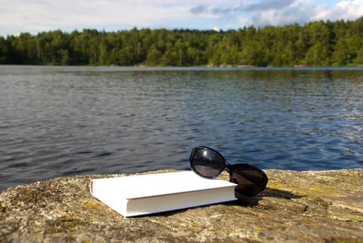 book and sunglasses lying on a stone in front of the sea symbolizing recreation