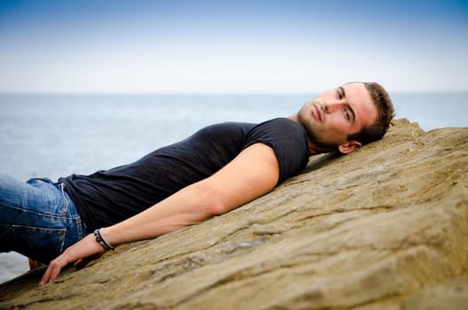 Attractive and fit young man laying on rock by the sea