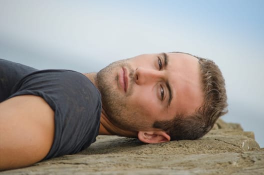 Handsome young man, brown eyes and hair, lying on rock