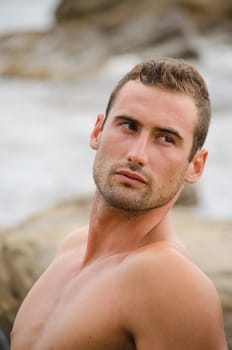 Shirtless and fit young man on rock by the sea looking away