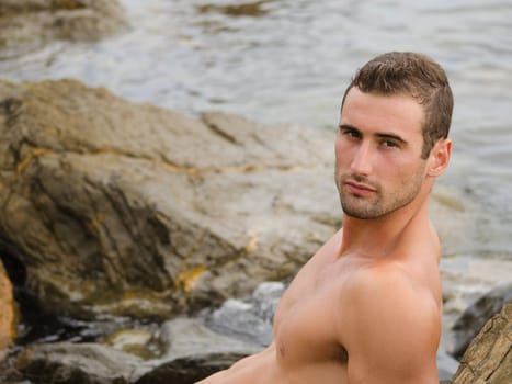 Shirtless and fit young man on rock by the sea or ocean