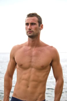 Attractive, shirtless muscular male model with sea behind