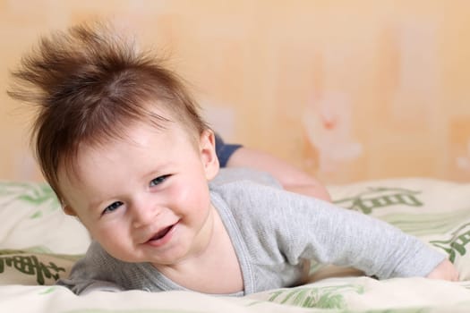 Portrait of a baby 4 months old lying on his belly with mohawk hairstyle.