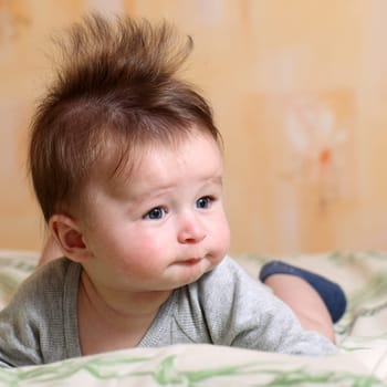 Portrait of a baby 4 months old lying on his belly with mohawk hairstyle.