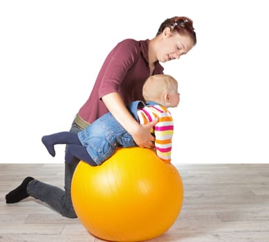 Mother exercising her young baby supporting it over a gym ball to stimulate muscle coordination and motion due to late development of motor skills