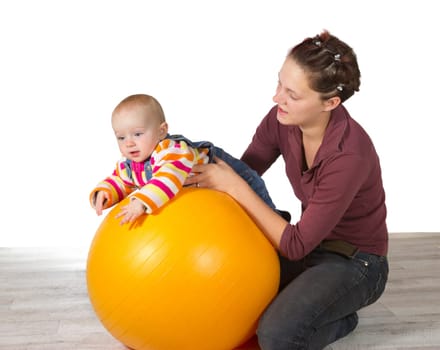 Baby with delayed motor activity development being supported on top of a yellow pilates ball by its caring mother in an effort to stimulate muscle response