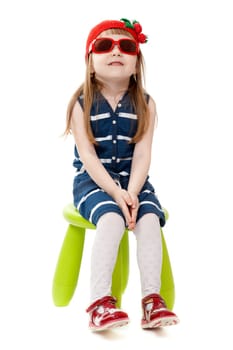 A girl of four years old sitting in a chair wearing sunglasses, isolate on white