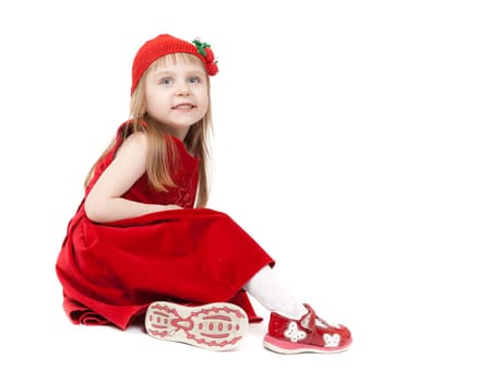 A little girl aged four years in a red dress and hat with strawberries sitting on the floor in the studio. Isolate on white