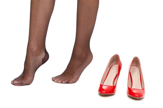 Beautiful female feet and near a pair of red high-heeled shoes. Isolate on white.