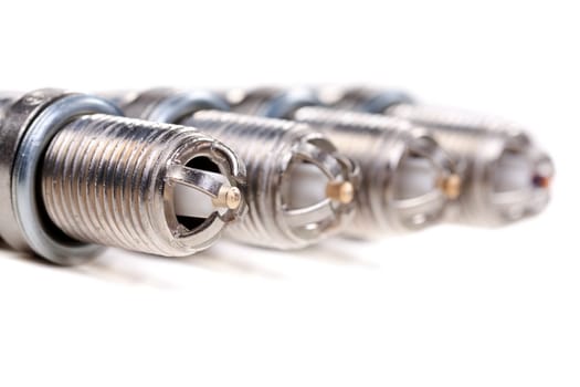 Set of four platinum spark plugs on a white background. Shallow depth of field.