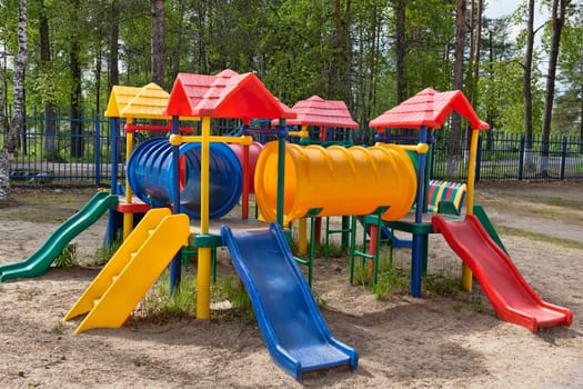 Plastic multi-colored children's playground in a pine park on a sunny day