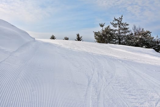 View on empty fresh-made downhill ski slope and mountains on a sunny day