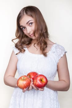 Beautiful young girl with three apples in their hands, in the studio on a gray background