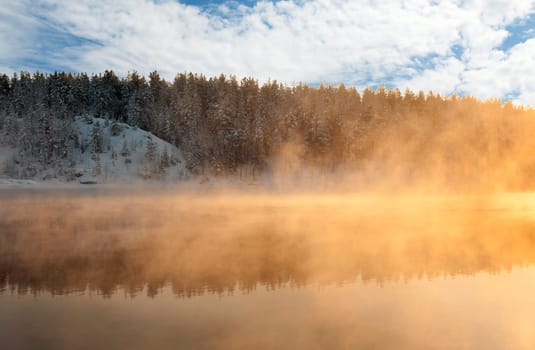 Reflection in the winter the lake with steam from the water in the setting sun