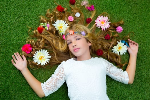 Blond spring children girl with flowers on hair over green grass floor