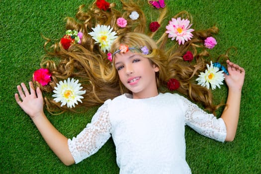 Blond spring children girl with flowers on hair over green grass floor