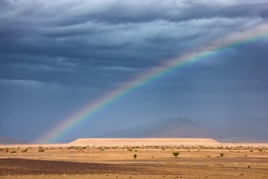 Dark clouds and rainbow in the Sahara desert.