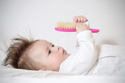 Portrait of a playing baby with a hairbrush, lying down on back