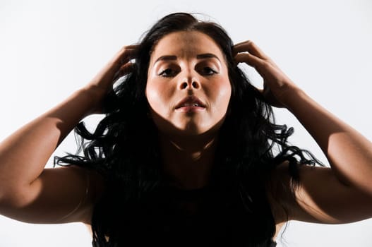 Head and shoulders shot of a young black-haired woman against a white background grabbing her hair with her fingers and putting her head back a little