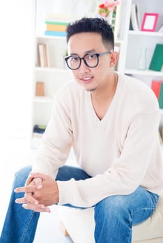 Southeast Asian male with spectacles sitting on sofa at home, indoor living lifestyle