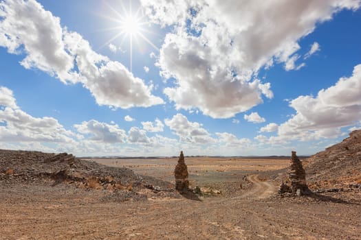 Stony desert landscape with sun and cloudy blue sky, Sahara desert, Morocco.