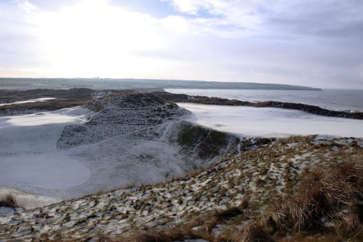 atlantic ocean beside a snow covered links golf course in ireland in snowy winter evening